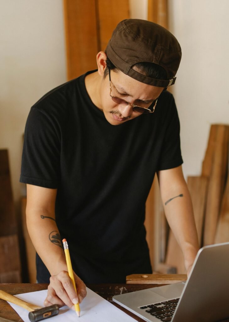 A craftsman in a workshop concentrates on planning a woodworking project with a laptop.